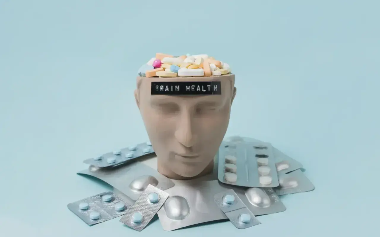 Testa di manichino piena di pillole, con la scritta "BRAIN HEALTH". Intorno, blister di psicofarmaci, suggerendo che il neurologo può prescrivere psicofarmaci.