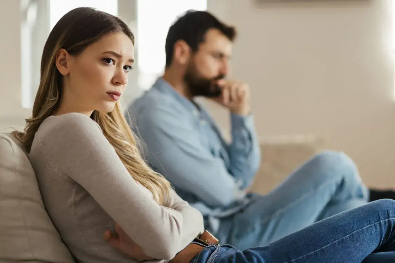 Coppia seduta sul divano, distanti. Lei guarda pensierosa, lui con la mano sul mento. Forse l'afefobia è sessualità, un muro invisibile tra loro.