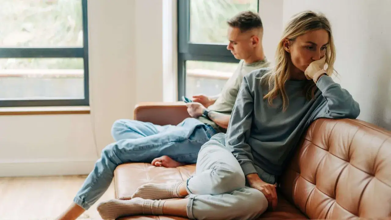 Coppia sul divano, lei pensierosa, lui al telefono. Un momento di distanza, dove si può non sentirsi capiti dal partner.