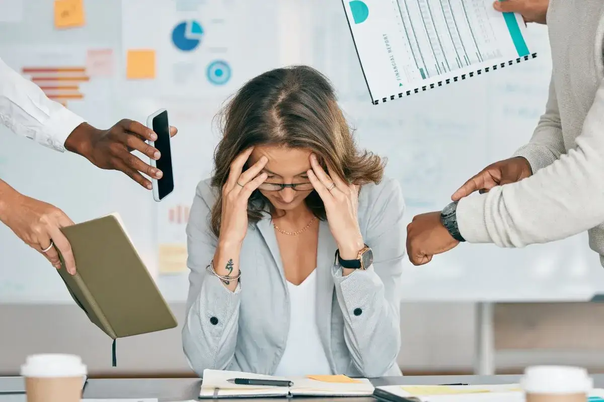 Donna sopraffatta da richieste lavorative, simile a chi vive con ADHD adulti testimonianze. Mani che porgono telefono, report e agenda.