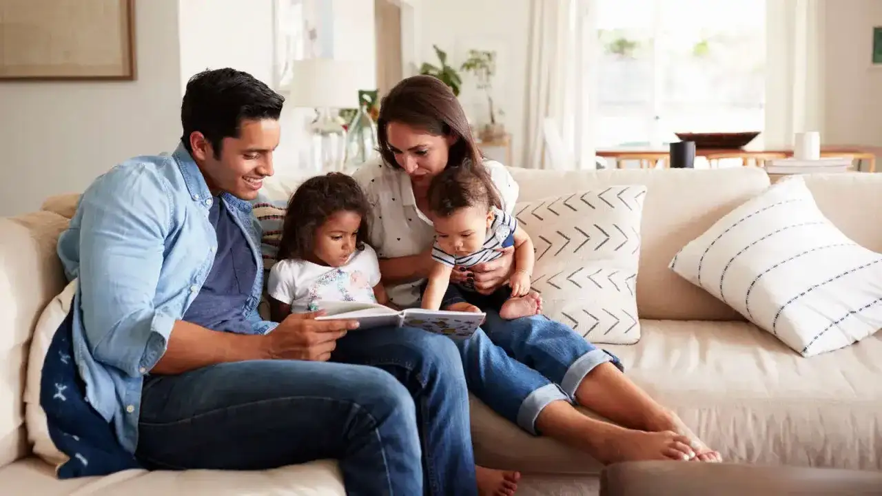 Famiglia unita sul divano, padre legge un libro ai figli. Un momento di serenità che ricorda l'importanza della psicoterapia sistemico relazionale per rafforzare i legami.