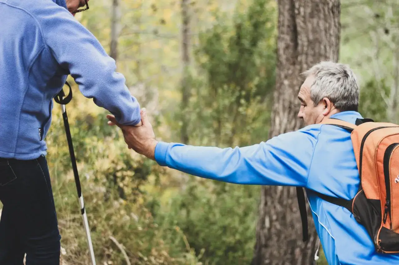 Uomo con zaino aiuta donna con bastoncini da trekking. Un gesto di supporto che evita di essere troppo disponibili psicologia.