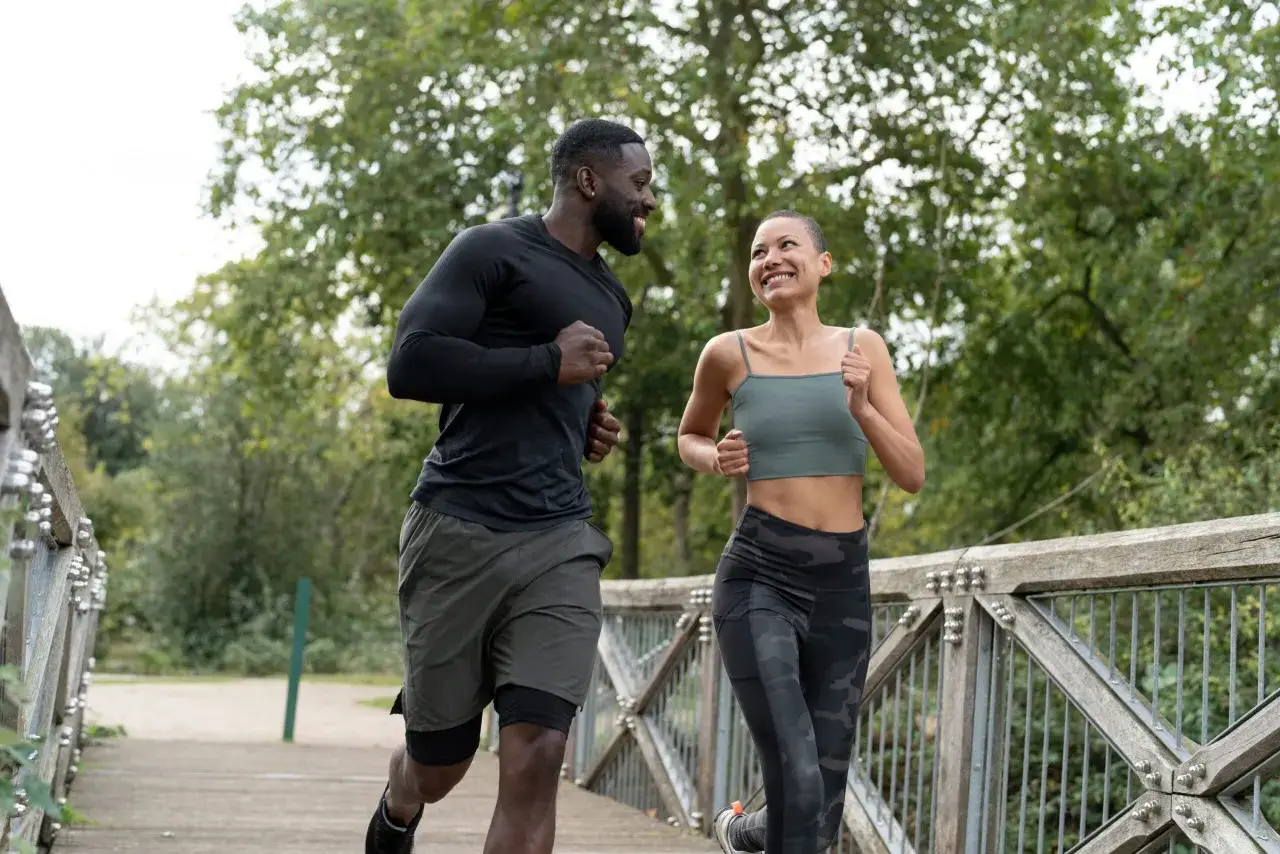 Coppia sorridente corre su un ponte in un parco. L'attività fisica è il miglior sport contro la depressione, un vero toccasana per corpo e mente.