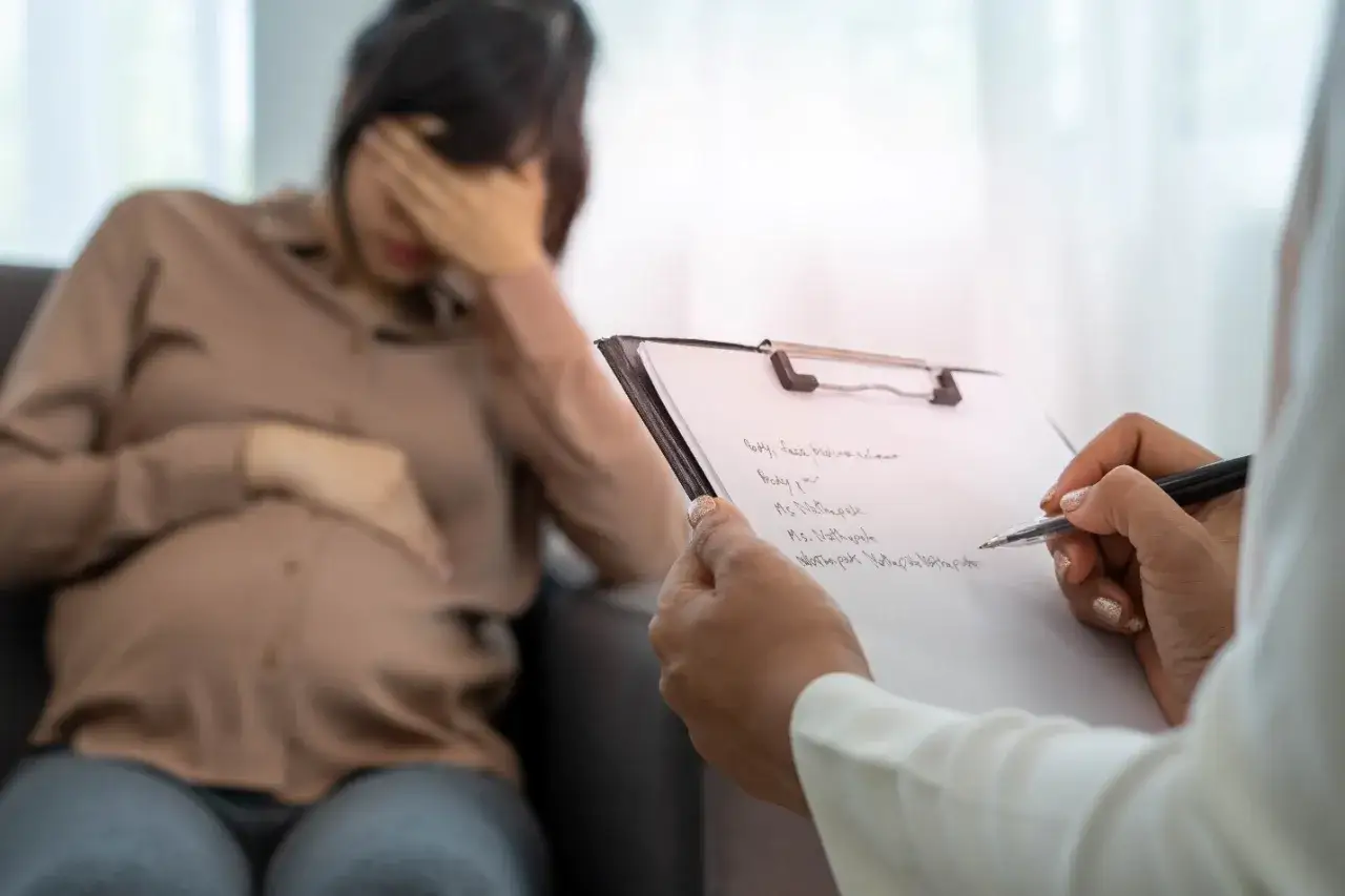 Donna incinta in crisi di pianto e nervosismo, parla con uno psicologo che prende appunti.
