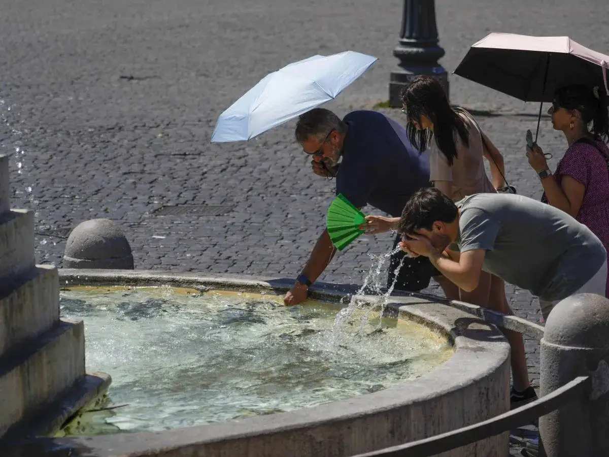 Persone cercano sollievo dal caldo e dalla depressione estiva rinfrescandosi in una fontana, con ombrellini a proteggere dal sole cocente.
