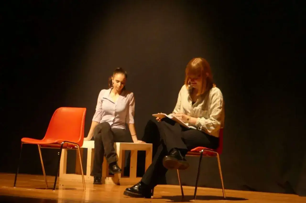 Due ragazze sul palco, una legge appunti, l'altra sembra pensierosa, forse per l'ansia da prestazione scolastica.