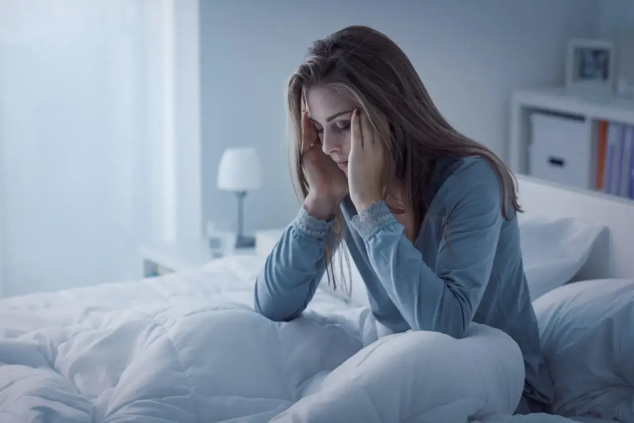 Donna a letto, con le mani sulle tempie, esprime sofferenza. L'autoerotismo e la depressione possono portare a momenti di profonda tristezza.