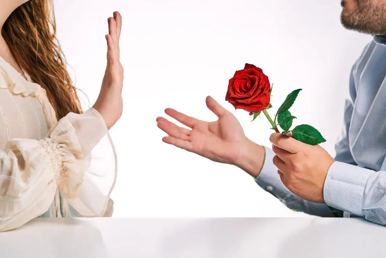 Una mano rifiuta una rosa rossa. Un uomo offre un fiore, ma lei alza la mano. Come superare un rifiuto in amore?