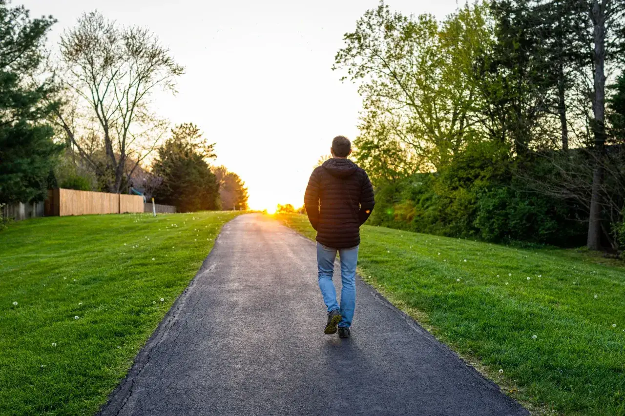 Un uomo cammina su un sentiero al tramonto, un passo alla volta, per imparare come riprendersi da un periodo di forte stress.